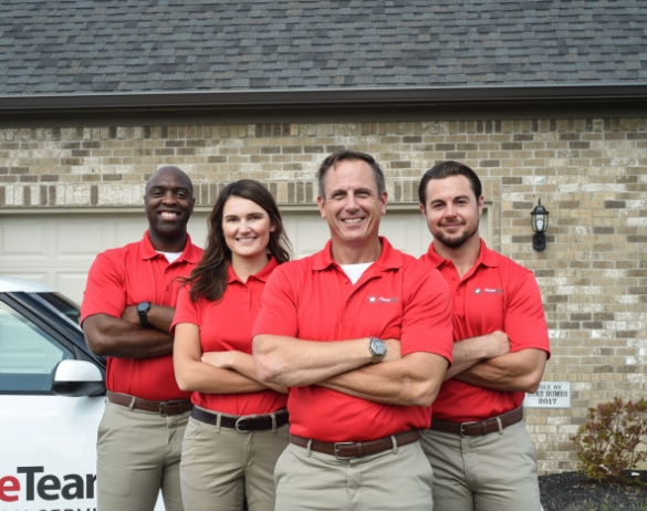 Four happy HomeTeam inspectors with folded arms and standing in front of a garage door