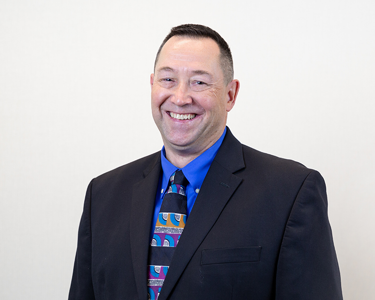 Professional portrait of Charlie Crout smiling in a brightly lit indoor setting.