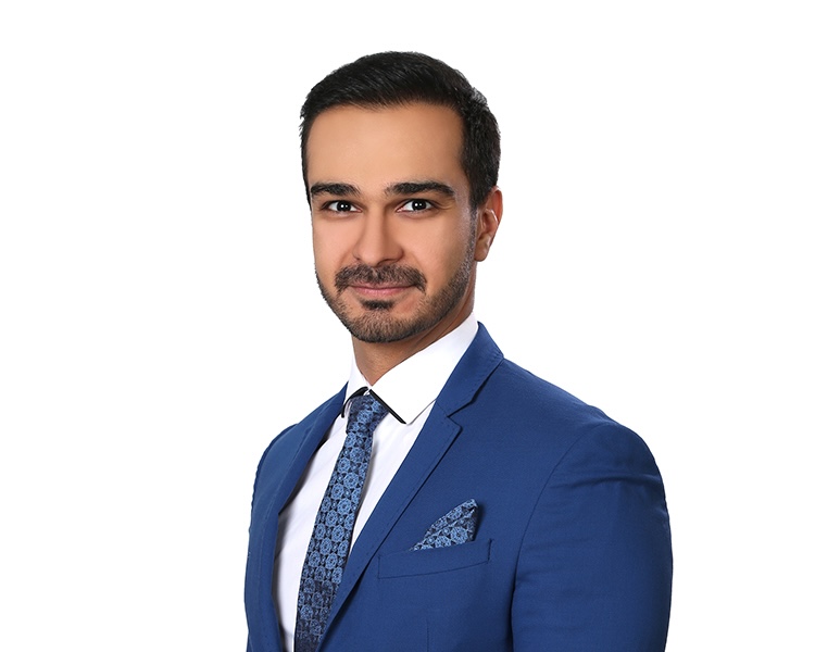 A professional portrait of a man with short dark hair and a beard wearing a bright blue suit, a white shirt, and a patterned blue tie and pocket square against a white background.
