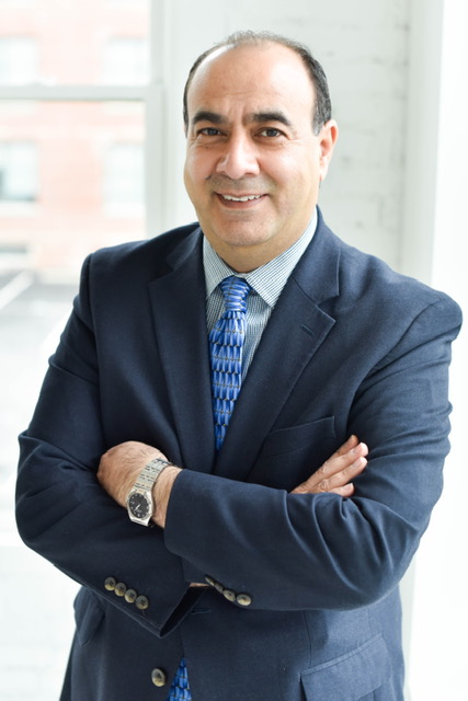 Professional portrait of Max Moarefdoustl smiling in a brightly lit indoor setting.