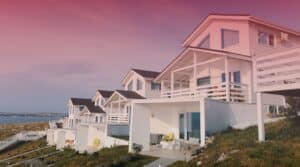 A row of modern white houses built on a grassy hillside along the coast.