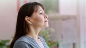 A woman in profile smiling comfortably and taking a deep breath indoors.